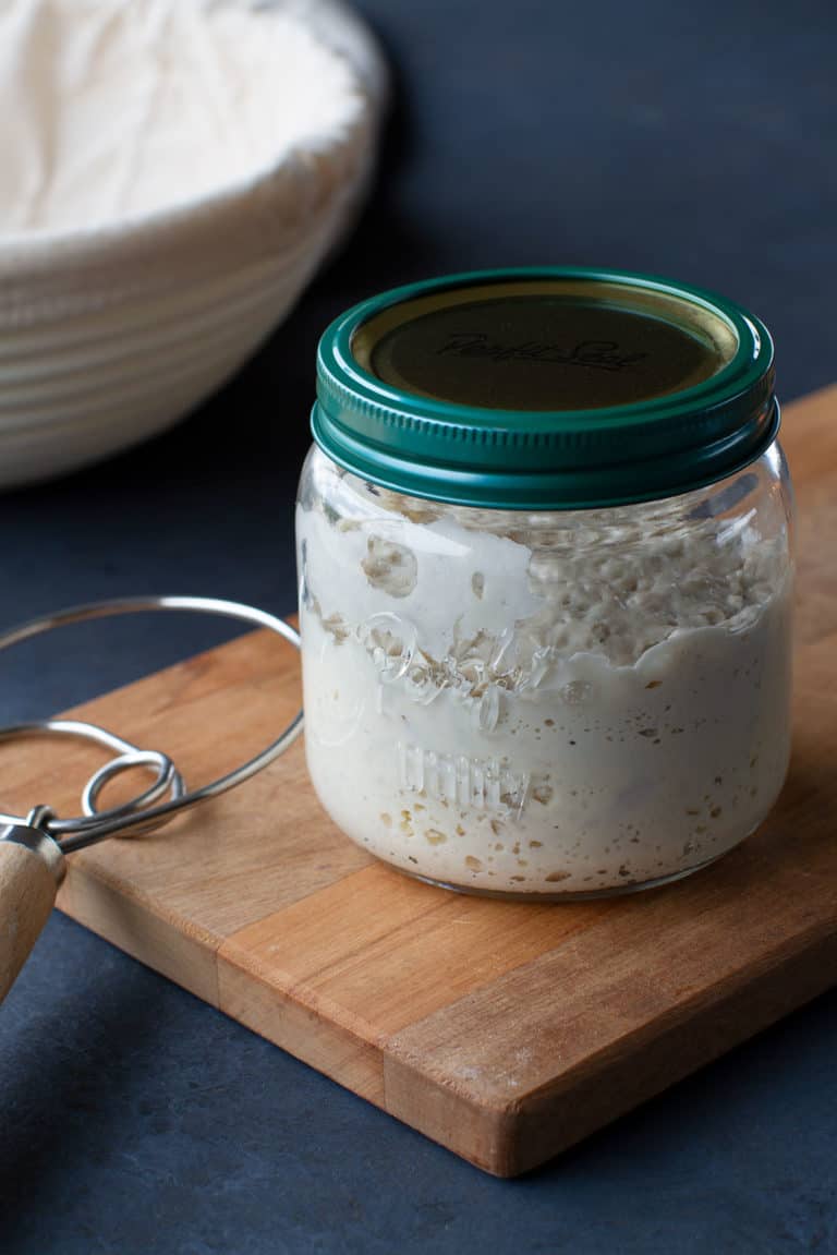 A glass jar of bubbly sourdough starter on a wooden board