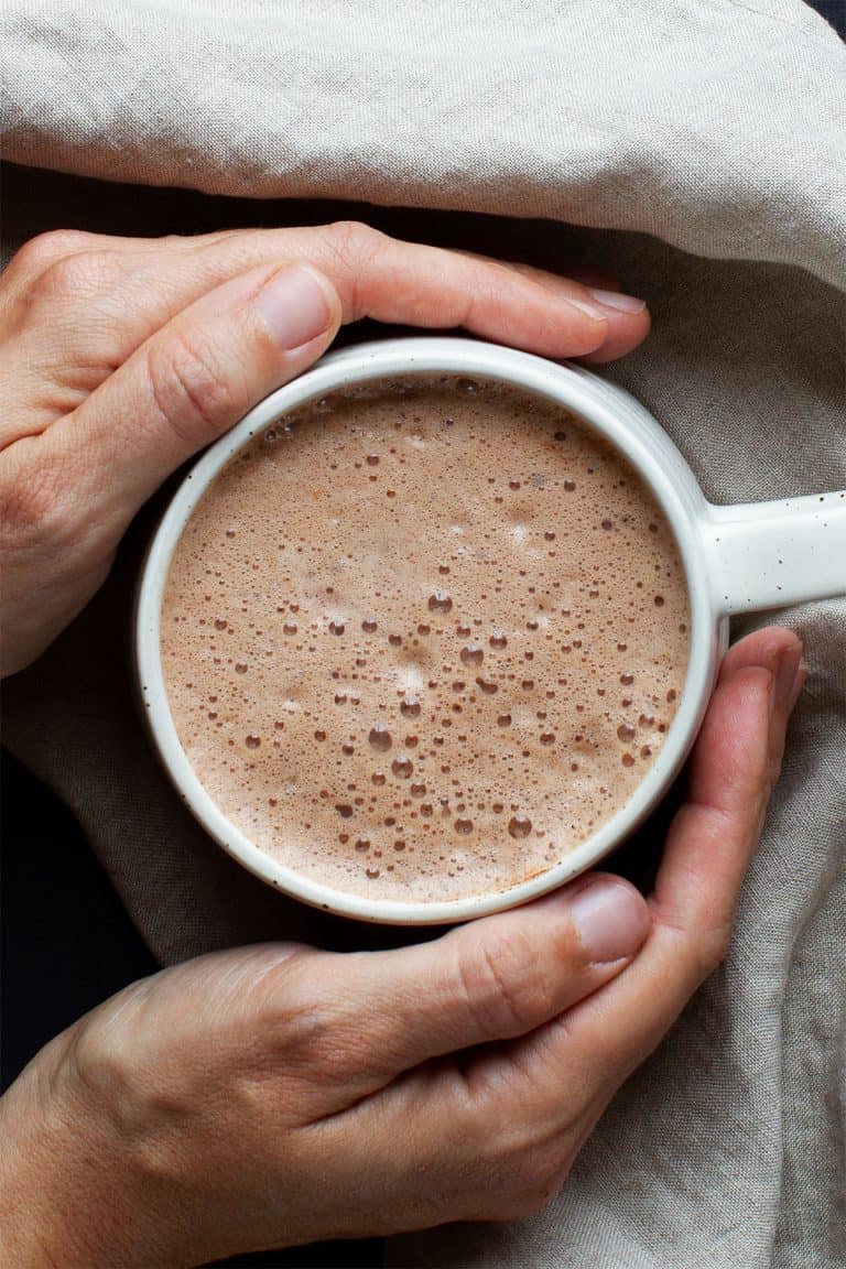 Hot chocolate in a white cup held by two hands.