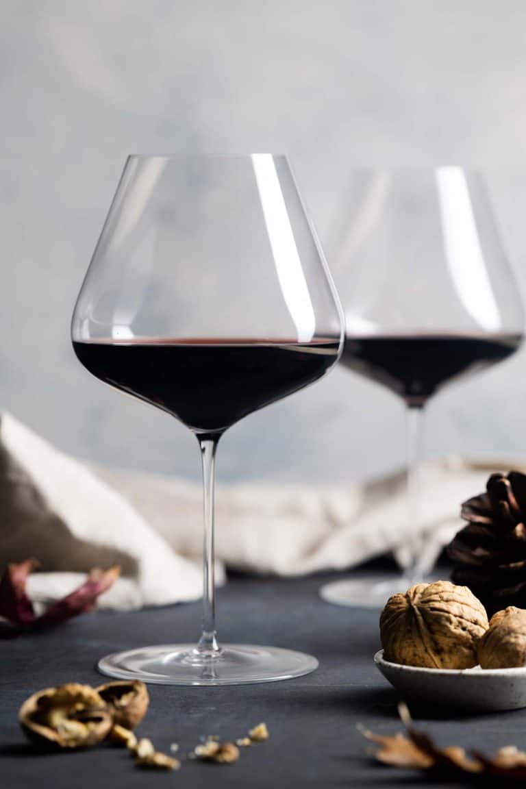 Two glasses of Pinot Noir wine in an Autumn setting showing leaves, walnuts, and a pinecone.