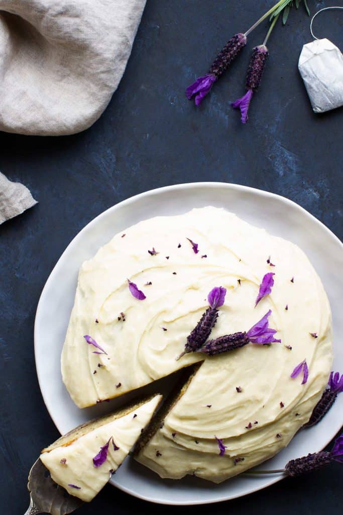 Bird's eye view of an earl grey lavender cake on a white plate next to lavender, a teabag and a linen tea towel.