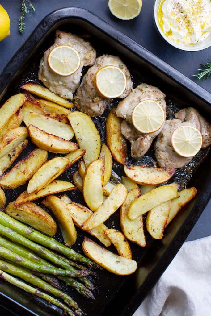 A sheet pan with chicken thighs, potatoes and asparagus.