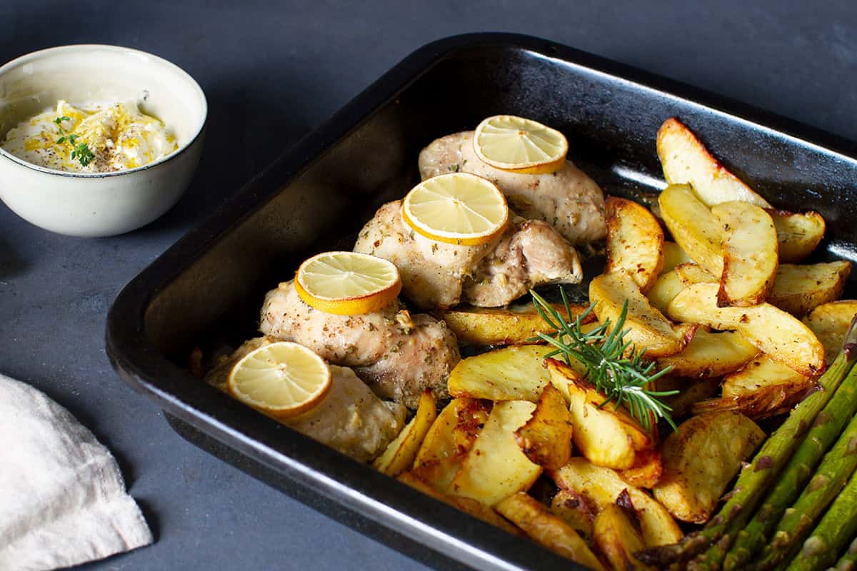 A sheet pan with chicken thighs, potatoes and asparagus.