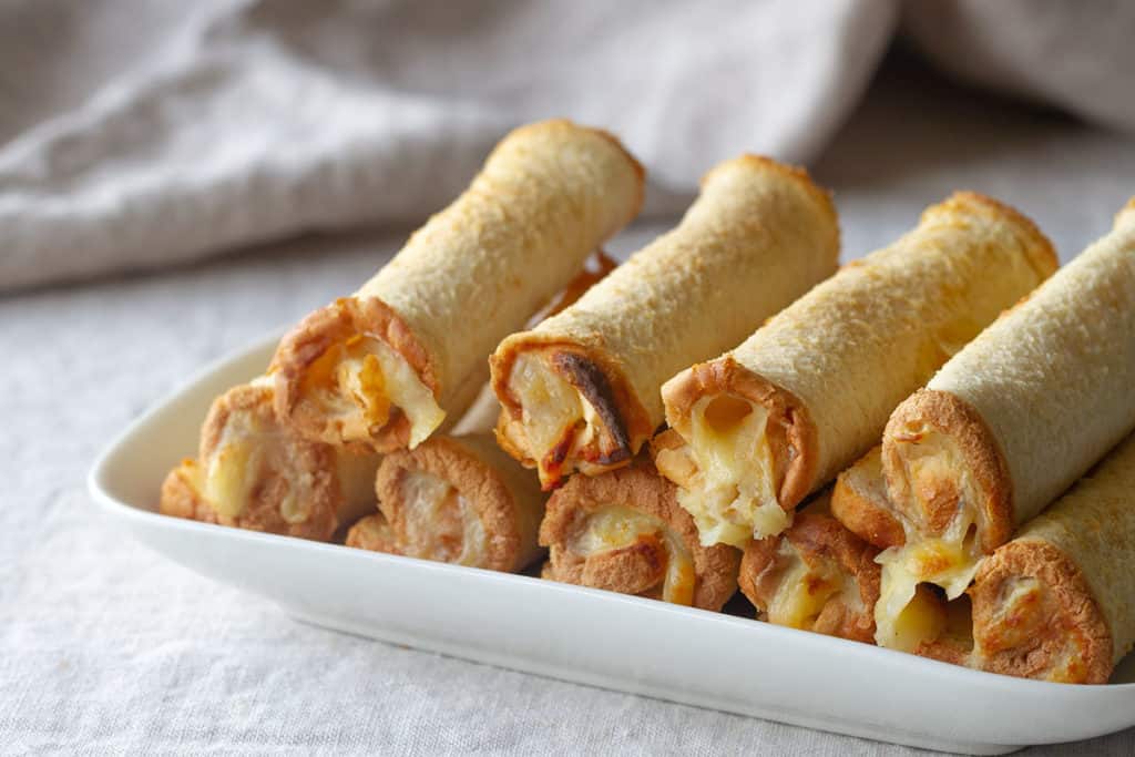 A stack of cheese rolls on a white plate.