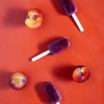 Three plum ice blocks and plum halves on a red background. Flatlay.