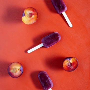 Three plum ice blocks and plum halves on a red background. Flatlay.