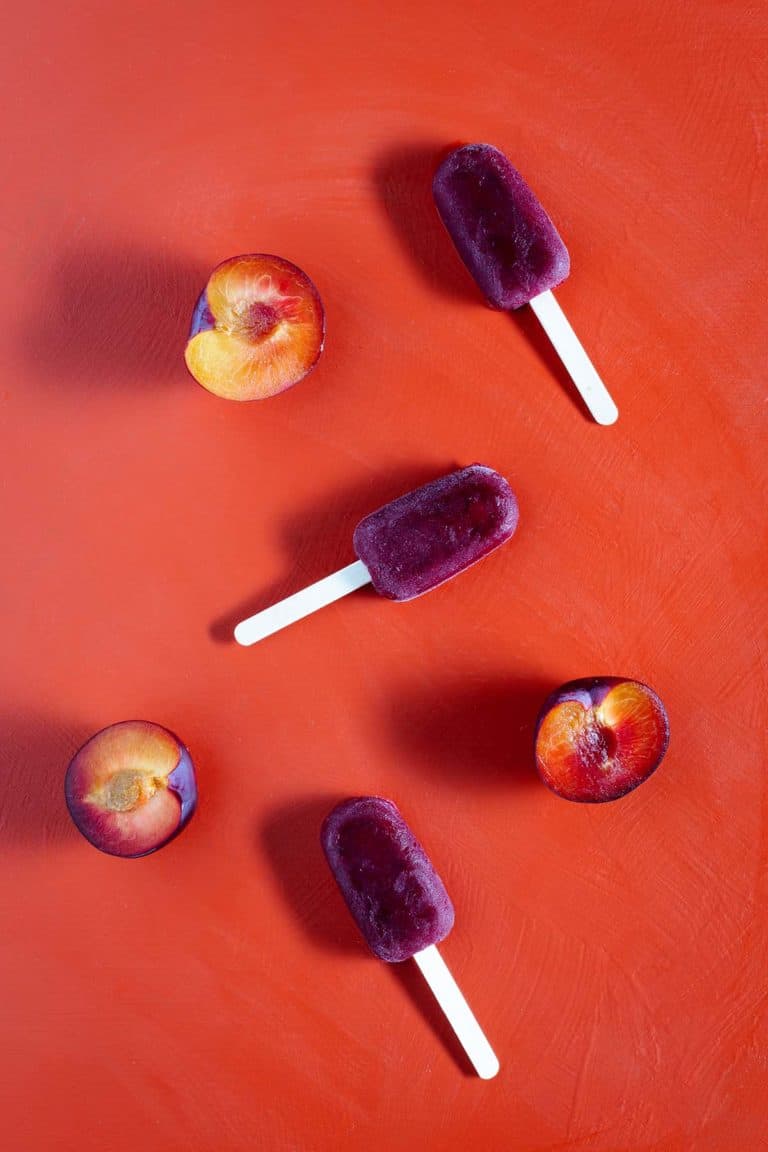 Three plum ice blocks and plum halves on a red background. Flatlay.