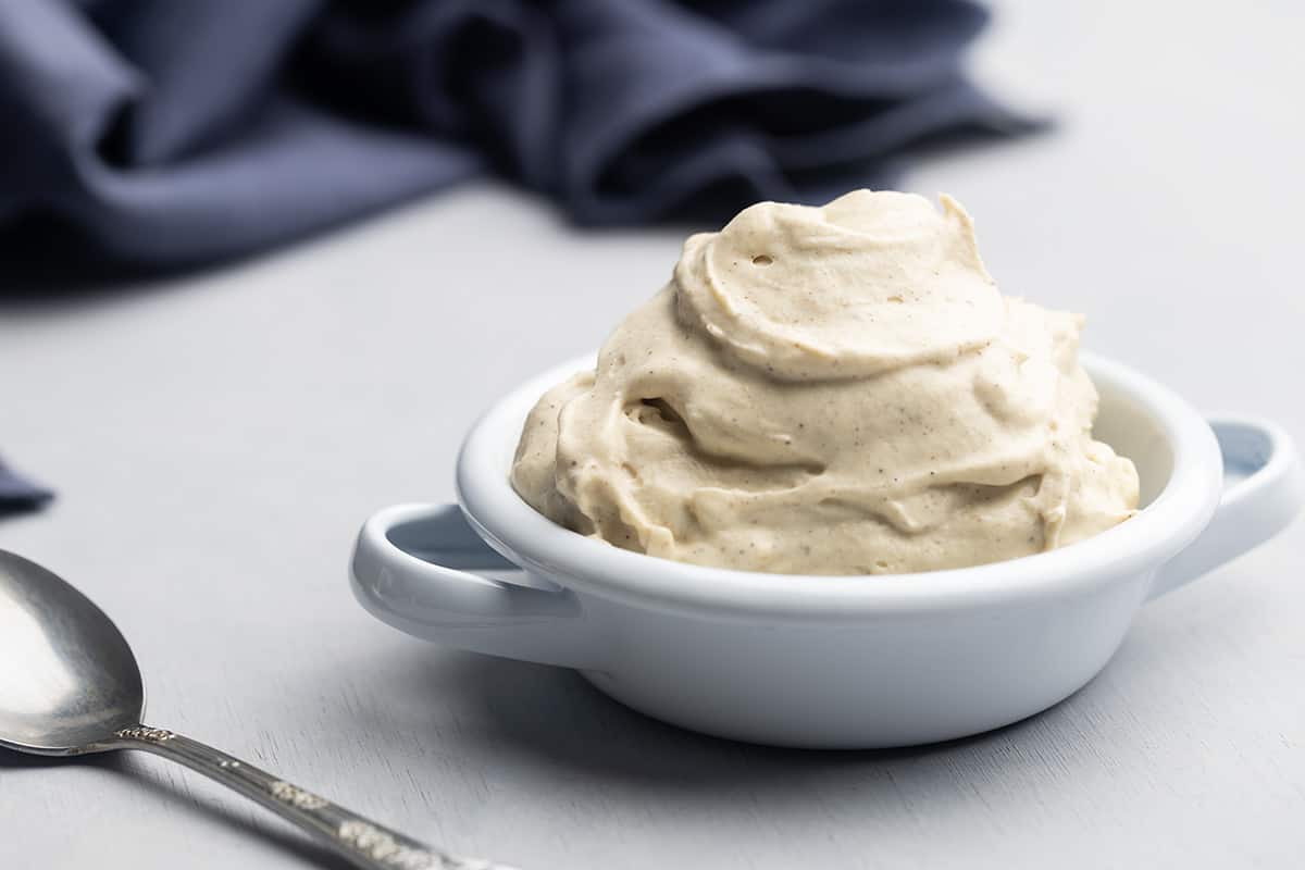 A bowl of whipped chantilly mascarpone next to a blue napkin and spoon.