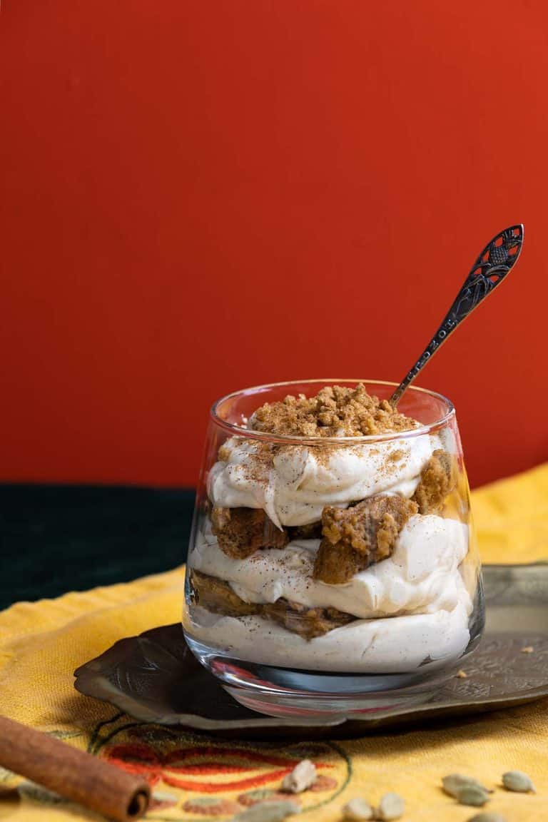 A chai tiramisu cup on a metal tray next to spices.