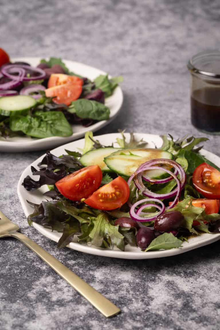 Mixed salads on small white side plates next to glass jar with vinaigrette.