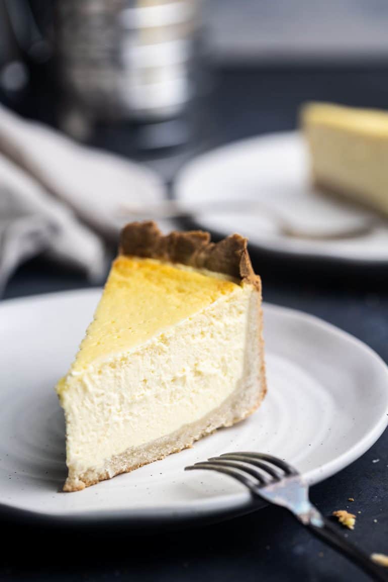 A slice of Rahmkuchen on a plate with a fork. Another slice is in the background blurred out.