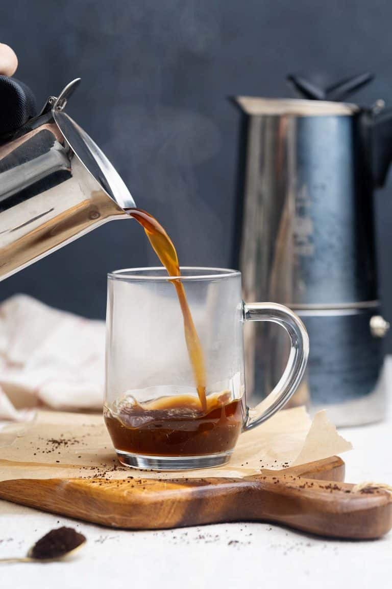 A Moka pot pouring coffee into a glass cup.