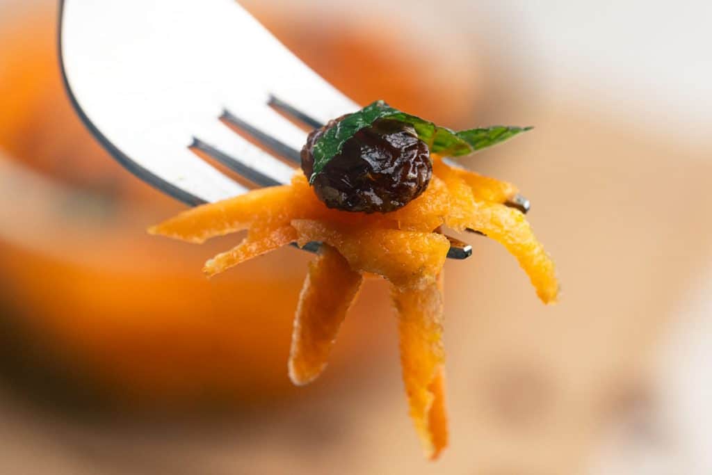 A close-up fork featuring a bite of raw carrot salad.
