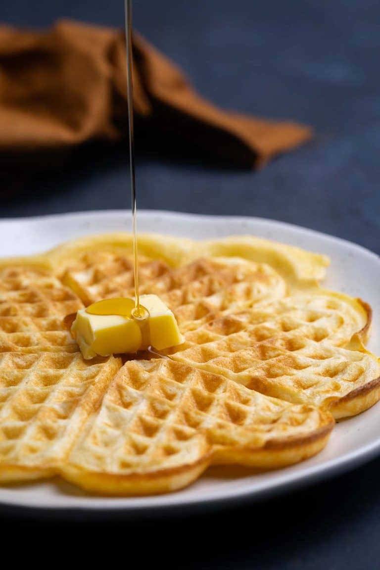 Homemade American waffles on a plate being drizzled with maple syrup.