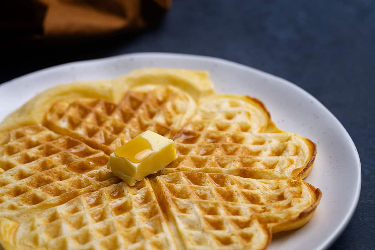 A fluffy American waffles on a plate being drizzled with maple syrup.