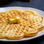 Homemade American waffles on a plate being drizzled with maple syrup.