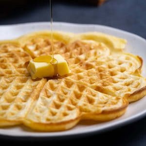 Homemade American waffles on a plate being drizzled with maple syrup.