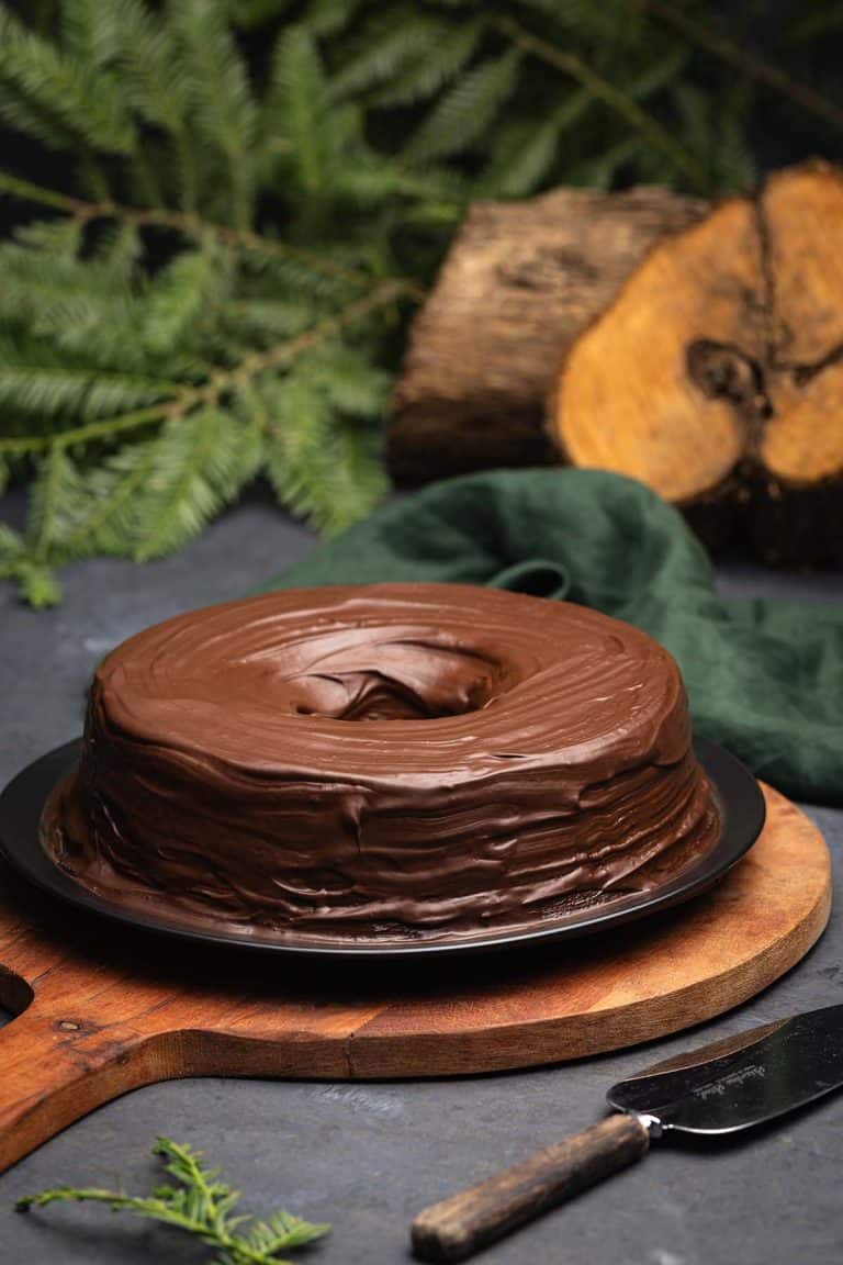 Baumkuchen on a wooden board next to a log and foliage.