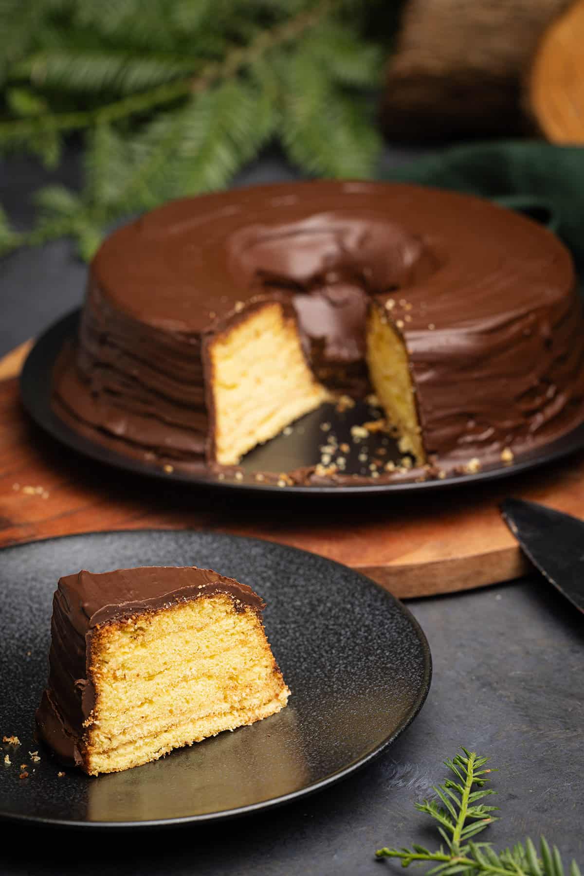 Baumkuchen on a wooden board next to a log and foliage.