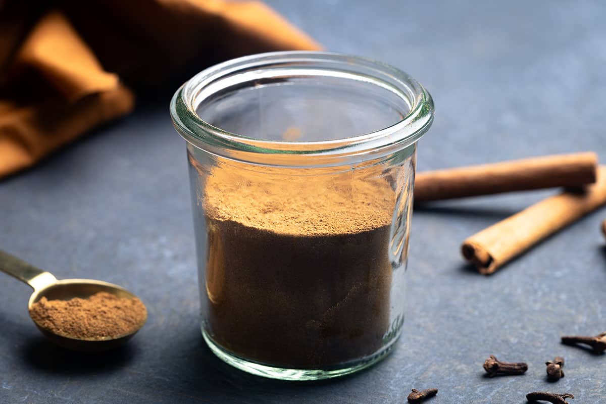 A jar of Christmas spice mix in a moody setting next to cinnamon quills.