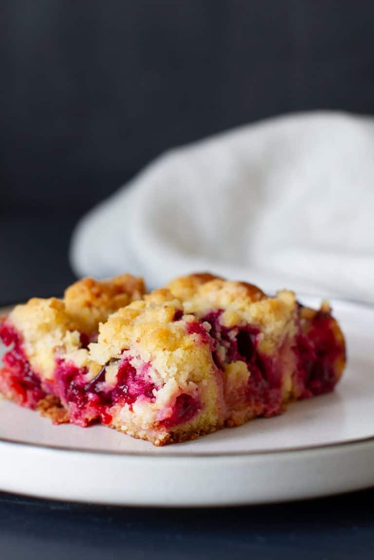 A piece of streusel cake with plums on a white plate.