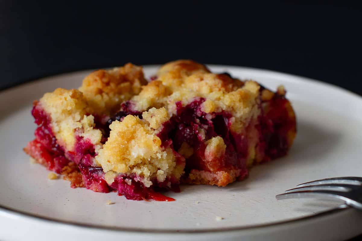 A piece of streusel cake with plums on a white plate.