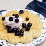 A whey waffle on a patterned plate with Greek yogurt and blueberries.