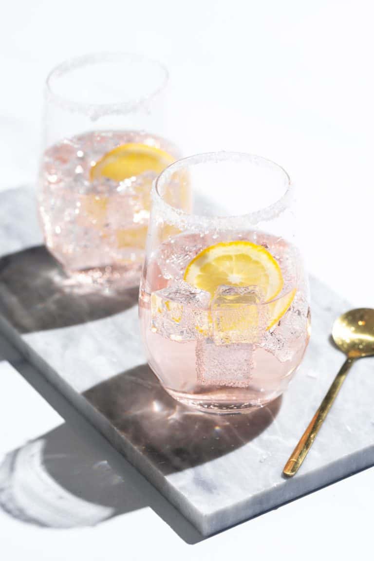 Two Rosé lemonade cocktails on a marble tray next to a golden spoon.