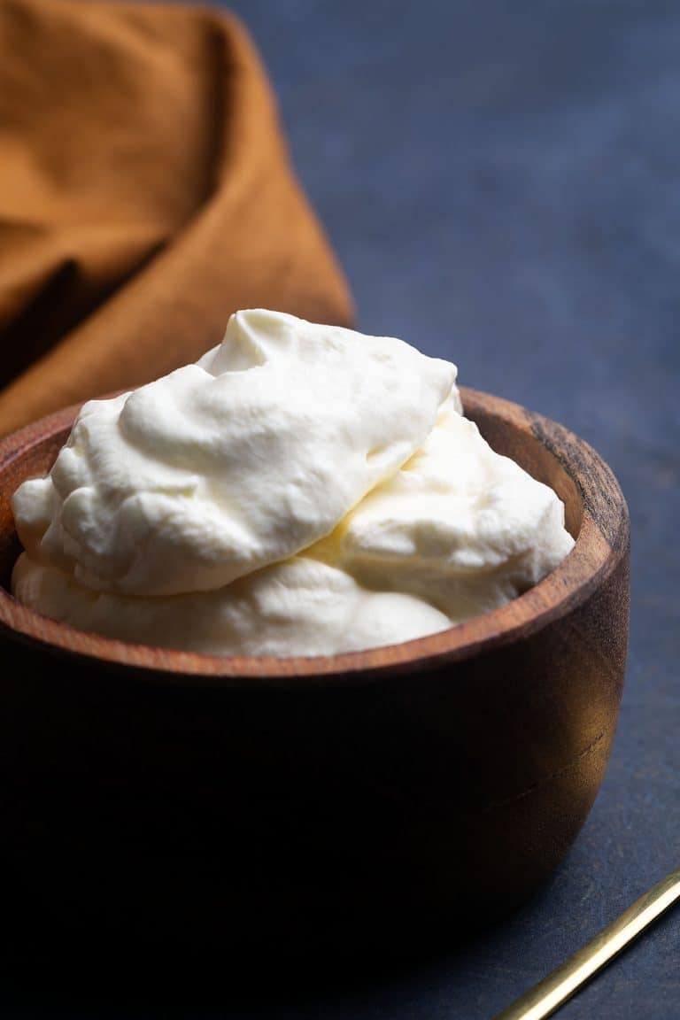 A wooden bowl filled with German whipped cream next to a golden spoon and napkin.