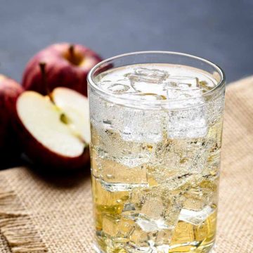 A glass of Apfelschorle on hessian fabric next to apples.