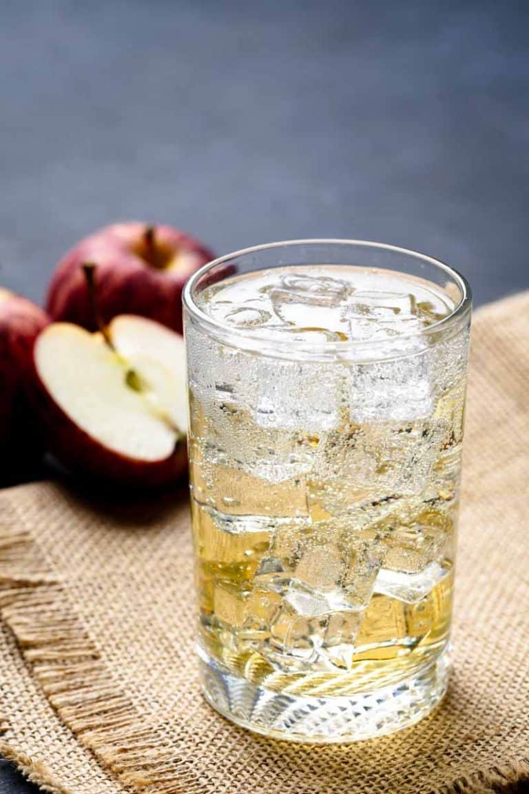 A glass of Apfelschorle on hessian fabric next to apples.