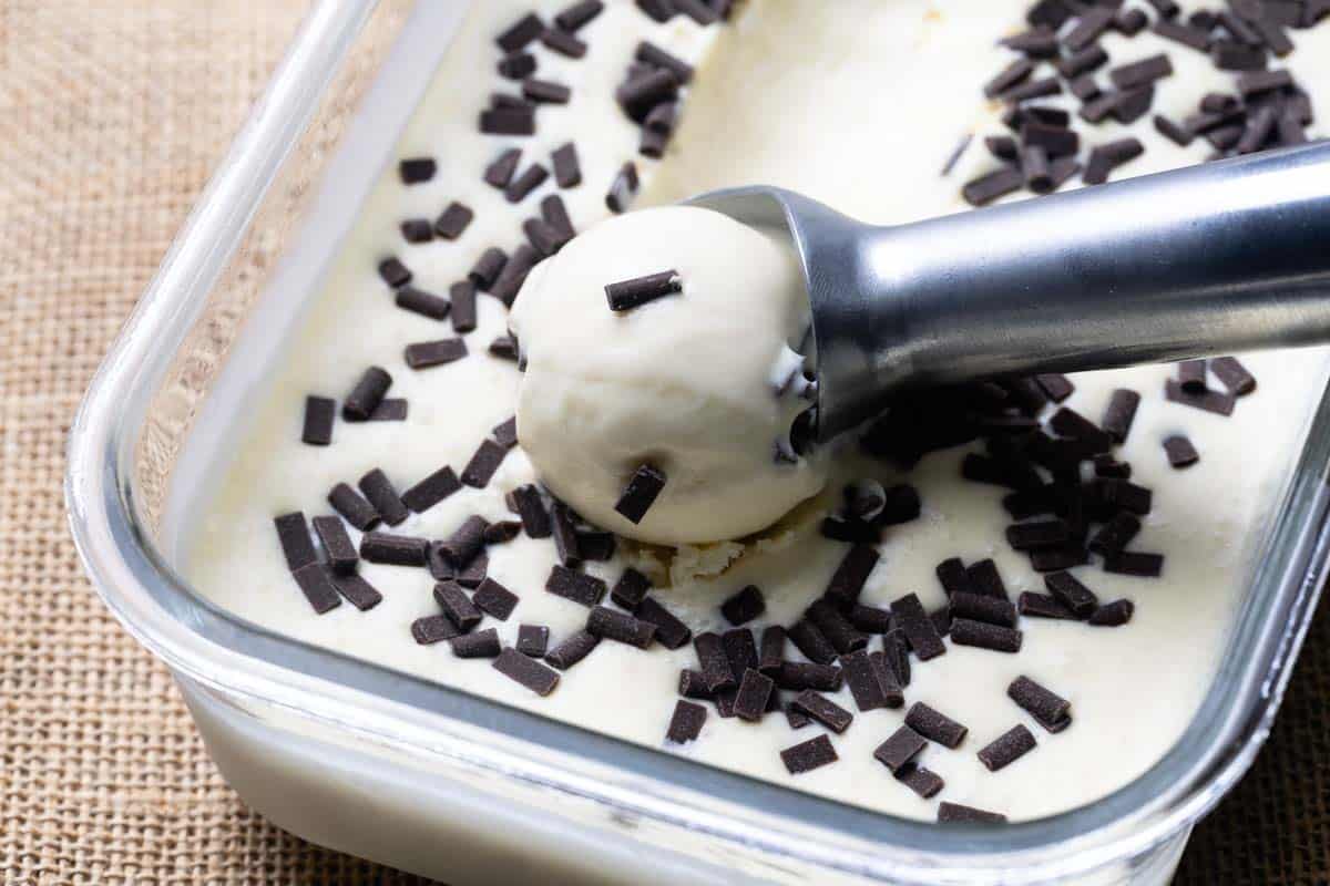 Straciatella ice cream in a glass container. A portion is being scooped.