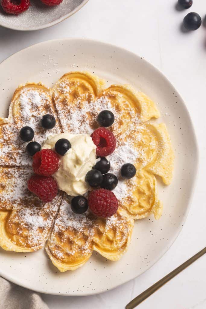 A waffles in a white plate with whipped cream and fresh berries.