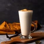 A hot vanilla drink in a glass cup on a wooden board. Moody scene.