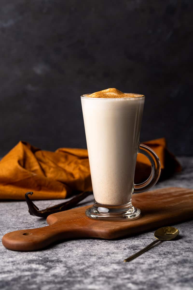 A hot vanilla drink in a glass cup on a wooden board. Moody scene.
