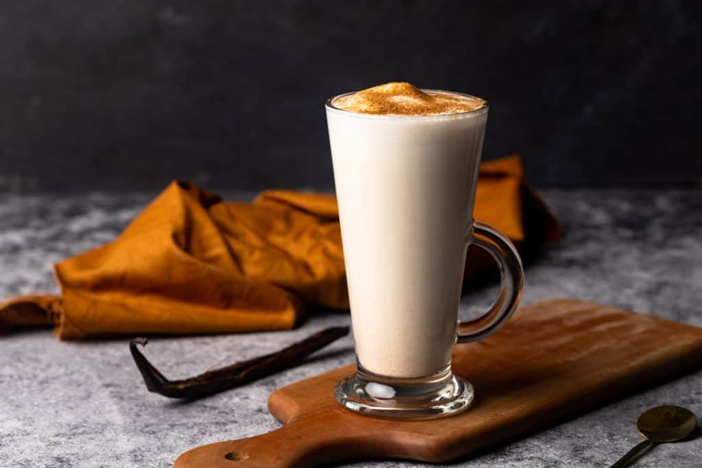 A hot vanilla drink in a glass cup on a wooden board. Moody scene.