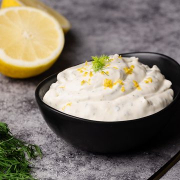 Lemon dill sauce in a black bowl next to lemons and dill.
