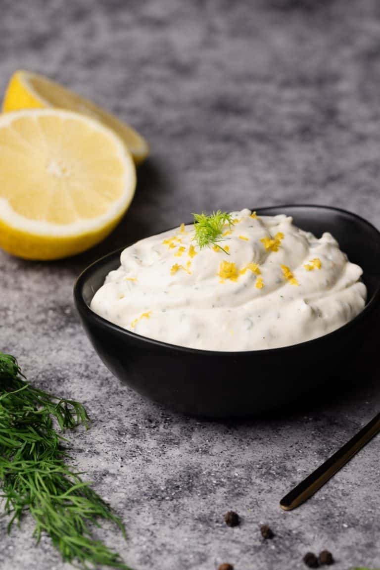 Lemon dill sauce in a black bowl next to lemons and dill.