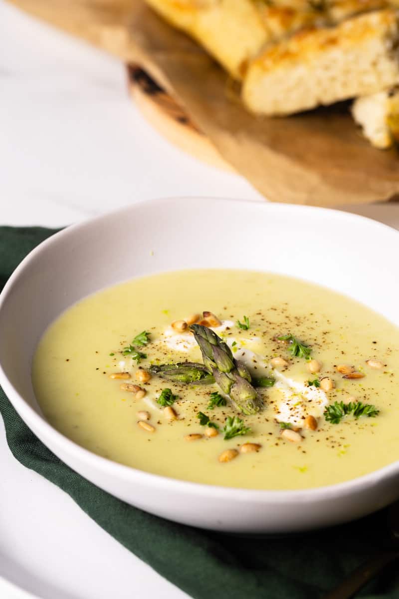 A bowl of asparagus potato soup next to some crusty bread.