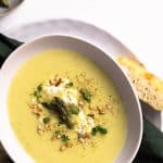 A bowl of asparagus potato soup next to some crusty bread. Flatlay.