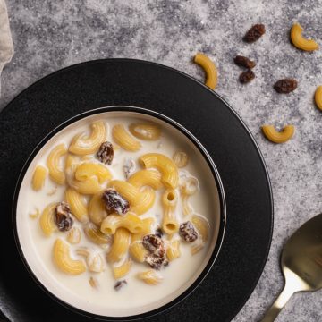 A bowl of milk soup with pasta on a black plate.