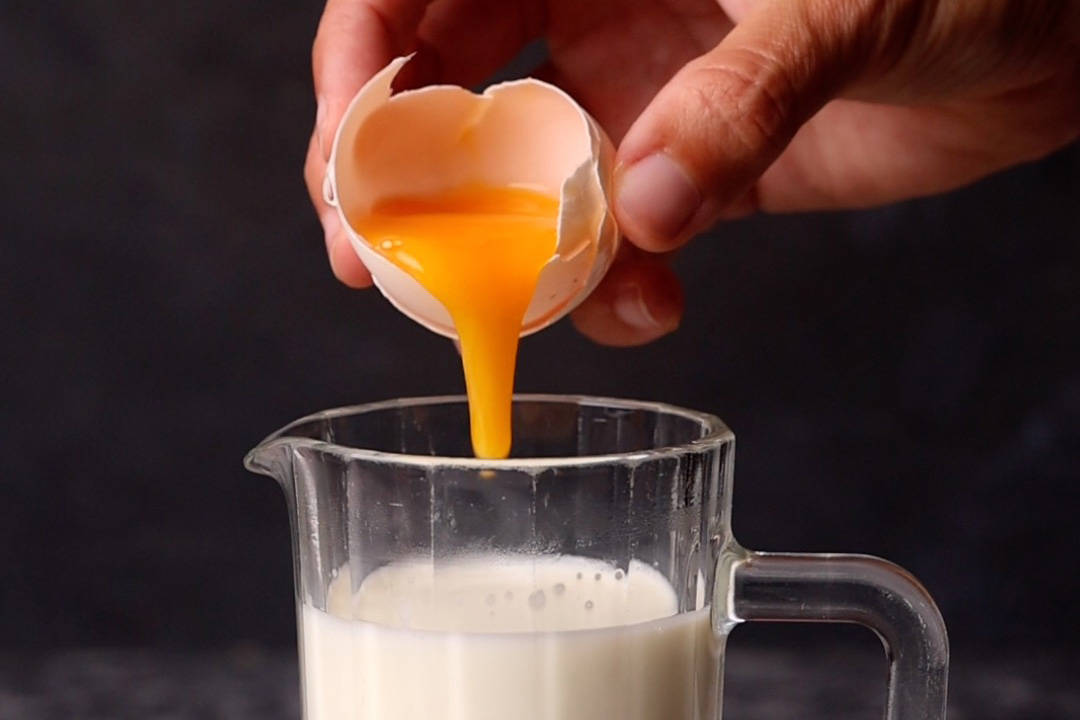 Egg yolk being dropped into a glass of hot milk.