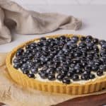 Lemon and blueberry torte on a wooden board next to a linen tea towel.