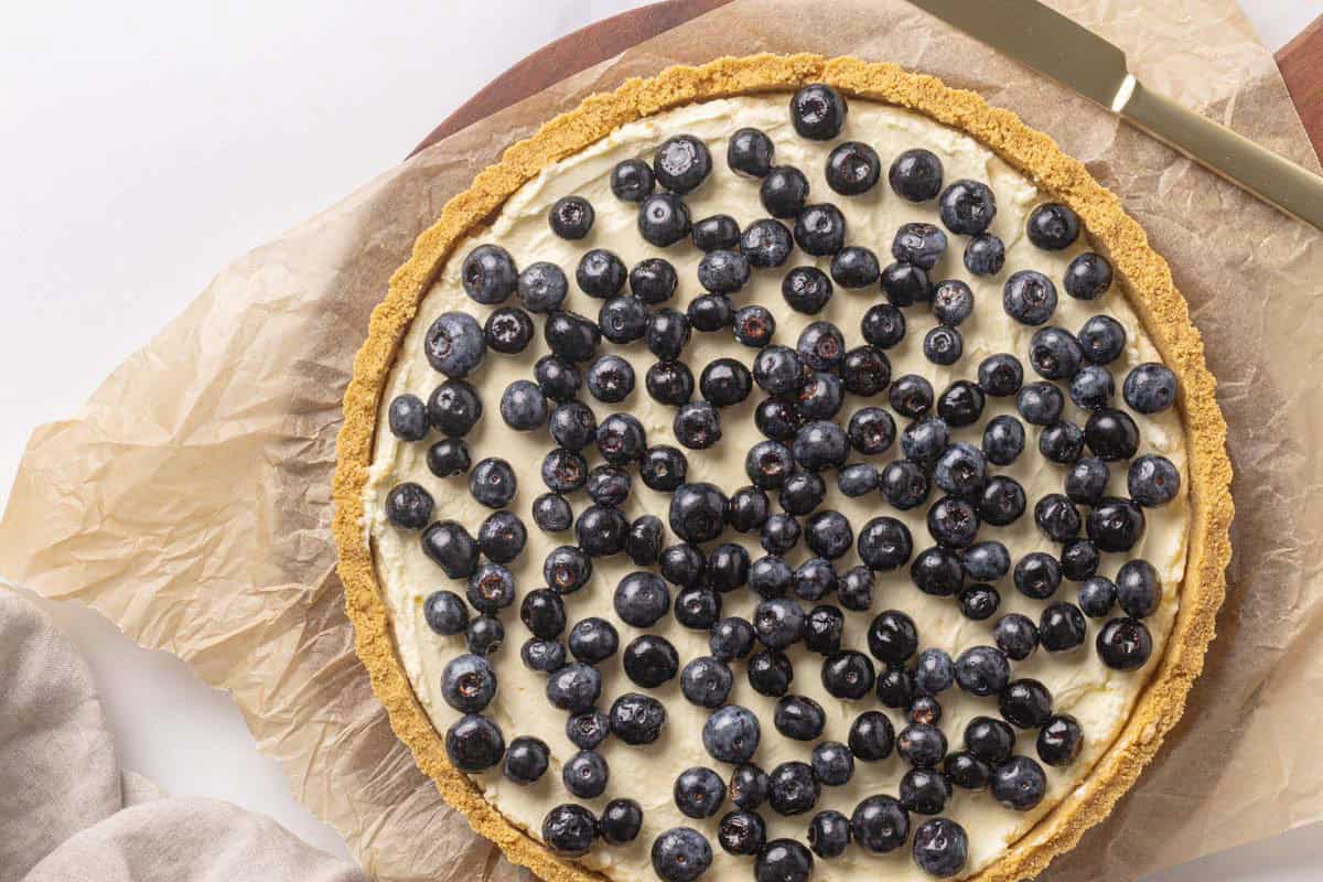 Lemon and blueberry torte on a wooden board next to a linen tea towel.