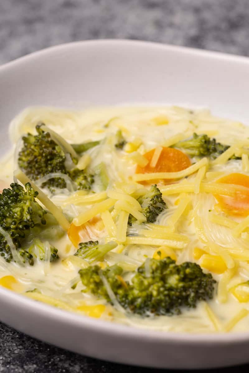 One white bowl filled with broccoli cheese soup with noodles.