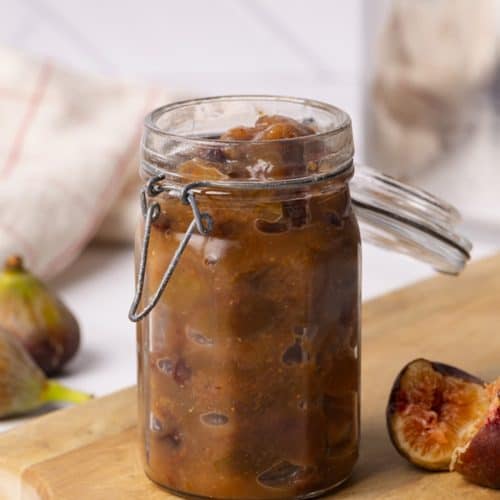 Fig chutney in a glass jar on a wooden board.