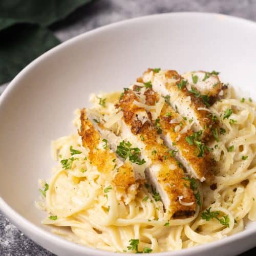 Breaded chicken on creamy linguine pasta in a white bowl next to green napkin.