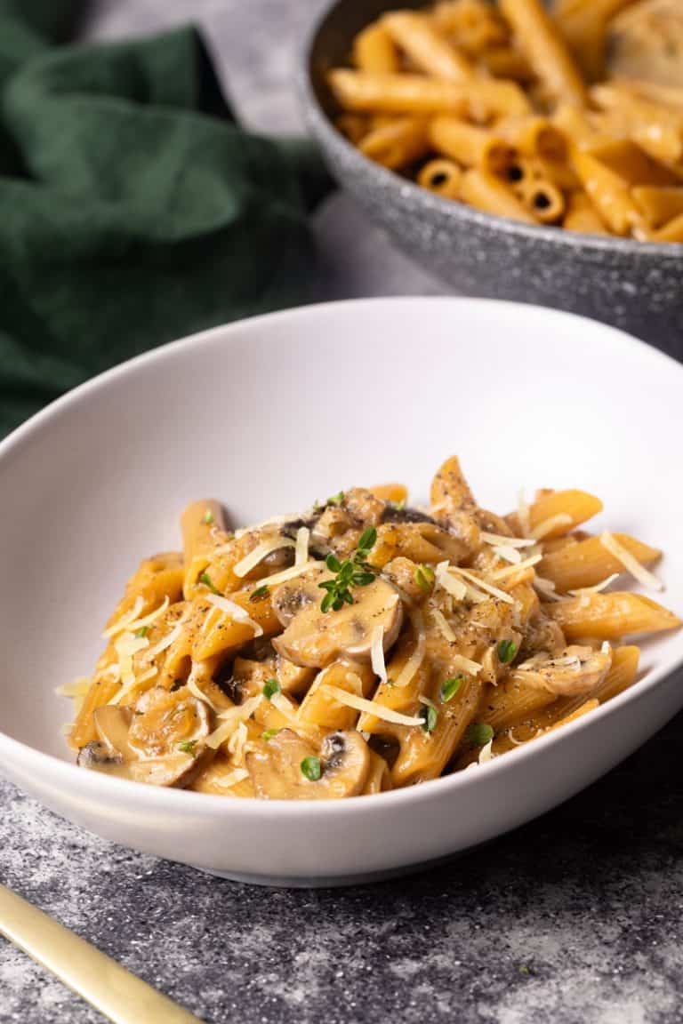 French onion pasta in a white bowl, next to a large pan and green napkin.