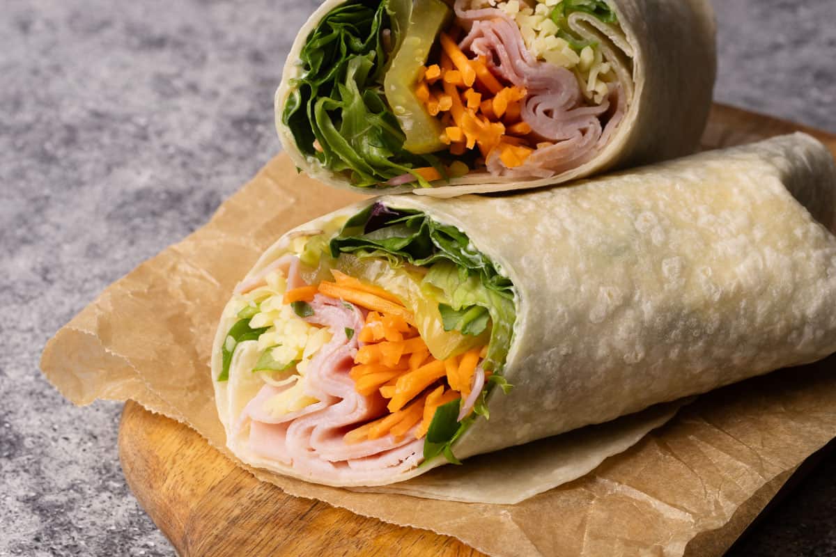 Ham and cheese wrap cut in half on a wooden board next to a green napkin.