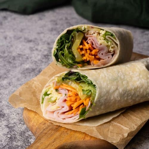 Ham and cheese wrap cut in half on a wooden board next to a green napkin.