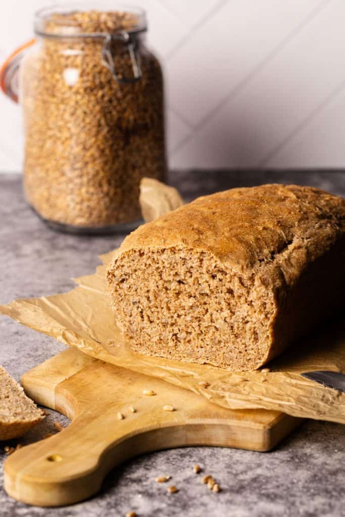 Spelt bread loaf on baking paper on a wooden board. One lice has been cut off.